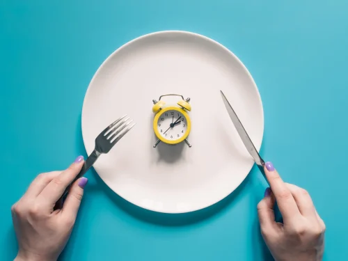 hands-holding-knife-fork-alarm-clock-plate-blue-background